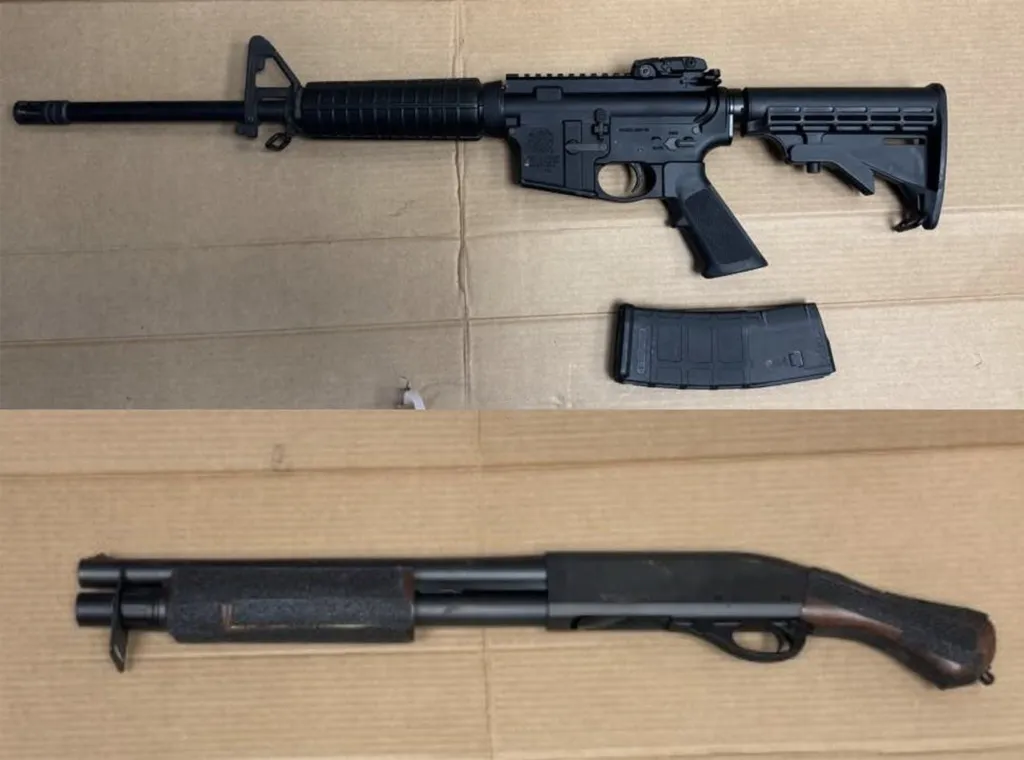 A black assault rifle with a magazine next to it, and a black shotgun, both laid on a cardboard surface.