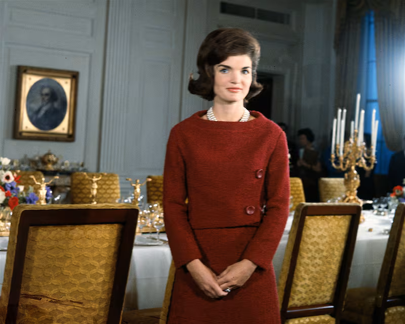 American First Lady Jacqueline Kennedy (1929 - 1994), in a red dress, stands in before a dining room table in the White House during the filming of a CBS News Special program called 'A Tour of the White House with Mrs. John F. Kennedy,' Washington DC, January 15, 1962. (Photo by CBS Photo Archive/Getty Images)
