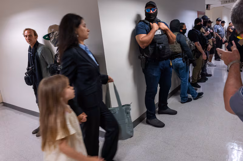 A woman and child walk past Federal agents as they patrol the halls of immigration court at the Jacob K. Javits Federal Building