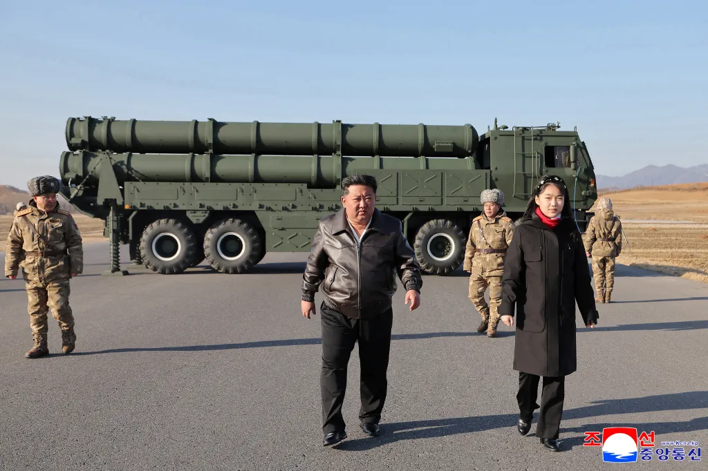 North Korean leader Kim Jong Un with his daughter and soldiers walking in front of a large-caliber multiple rocket launcher.