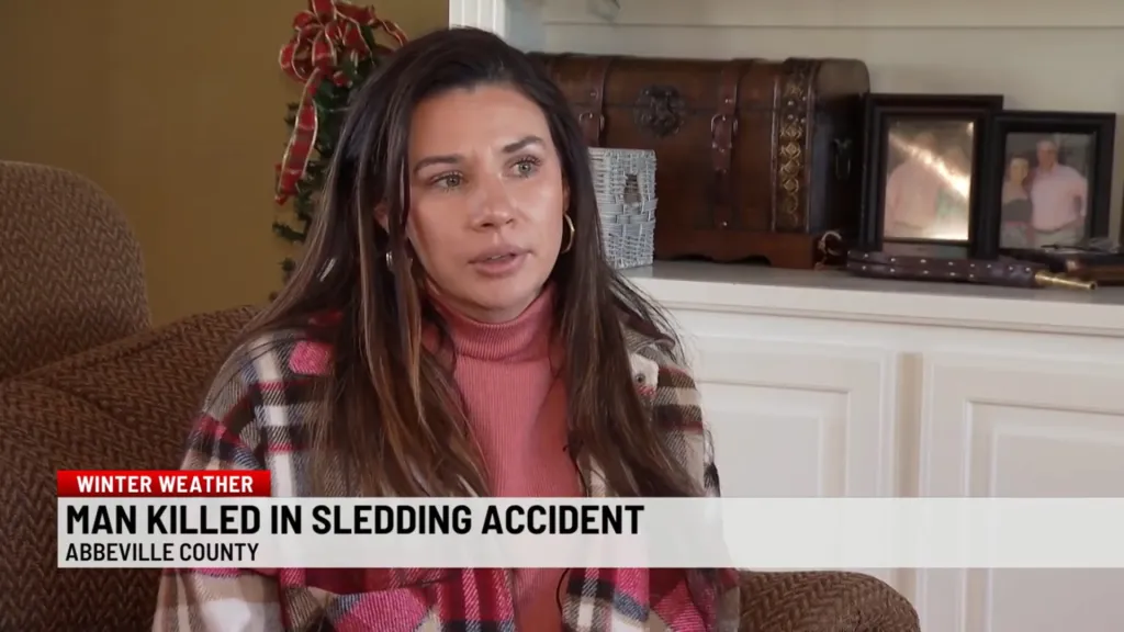 A woman in a pink turtleneck and plaid jacket is interviewed, with a news chyron reading