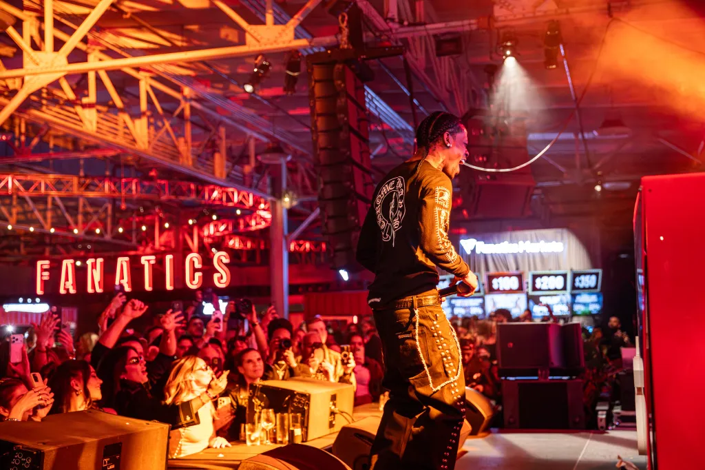 A musician performs on stage under red lights in front of a crowd with a 