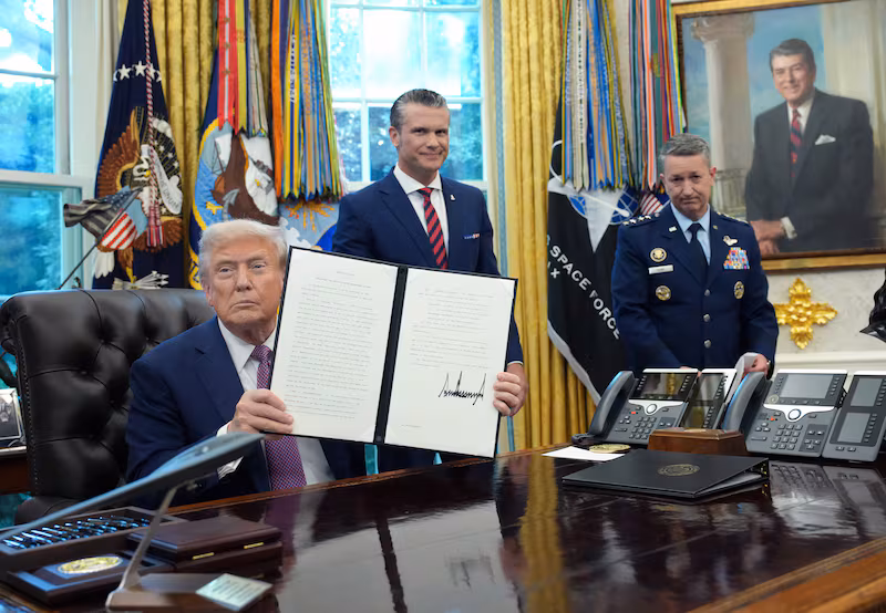 President Donald Trump displays a signed executive order renaming the Department of Defense as the Department of War as U.S. Defense Secretary Pete Hegseth (C) and Chairman of the Joint Chiefs of Staff Air Force Gen. Dan Caine (R) look on during a press availability in the Oval Office of the White House on September 05, 2025 in Washington, DC.