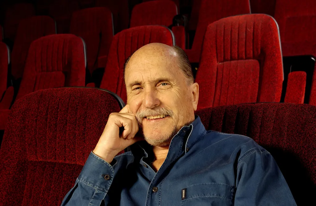 Actor Robert Duvall smiles in a movie theater, surrounded by red seats.