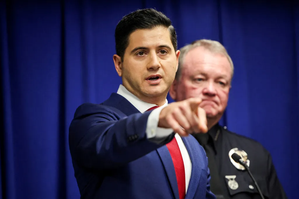 Acting United States Attorney Bill Essayli points forward while speaking at a press conference, with Los Angeles Police Chief Jim McDonnell behind him.