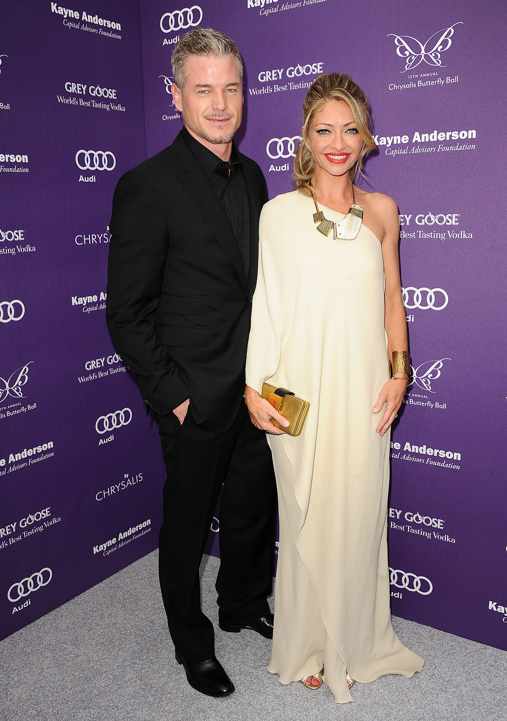 Eric Dane and Rebecca Gayheart posing together on a purple carpet with sponsor logos for the 12th annual Chrysalis Butterfly Ball.