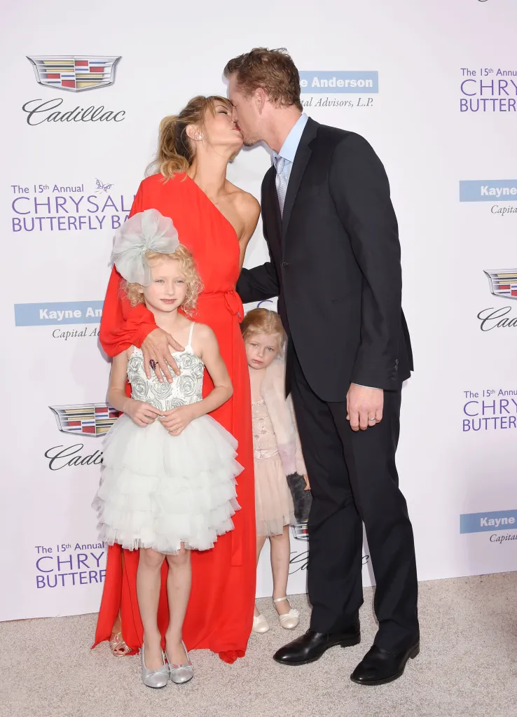Rebecca Gayheart-Dane in a red dress kisses Eric Dane in a suit, while their daughters Georgia Dane and Billie Beatrice Dane stand beside them at the Chrysalis Butterfly Ball.