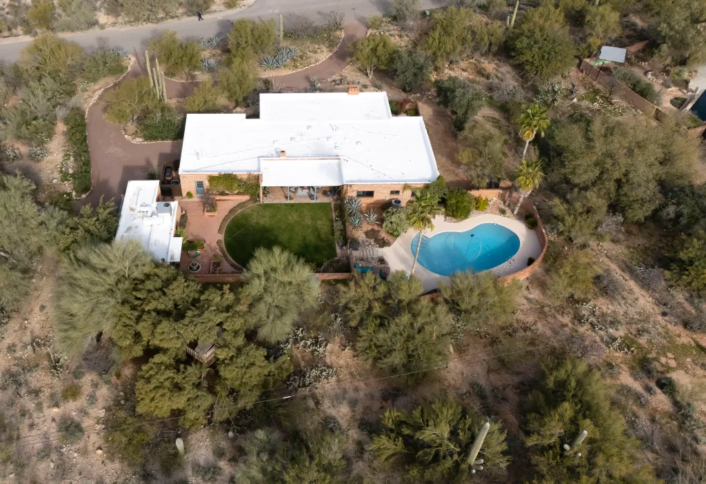 Aerial view of Nancy Guthrie's house in Tucson, Arizona, with a white roof, brick walls, and a kidney-shaped pool in the backyard surrounded by desert landscaping.