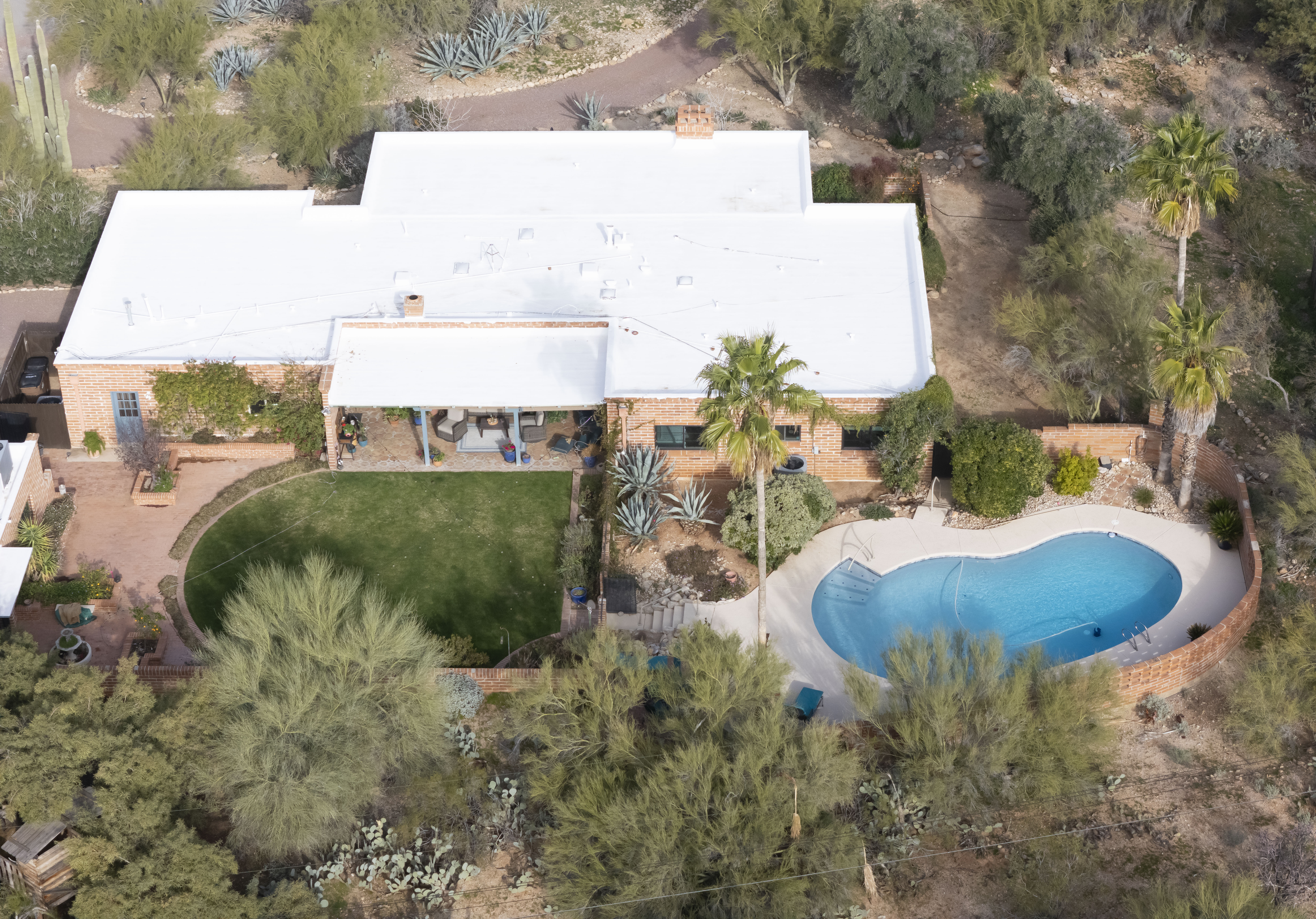 Aerial view of Nancy Guthrie's house in Tucson, Arizona, which has a white roof, brick walls, a green lawn, and a blue swimming pool in the backyard.
