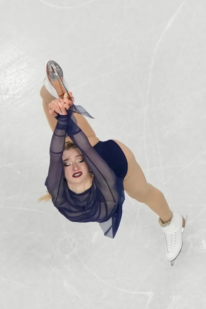 Amber Glenn performing a figure skating move on ice, viewed from above.