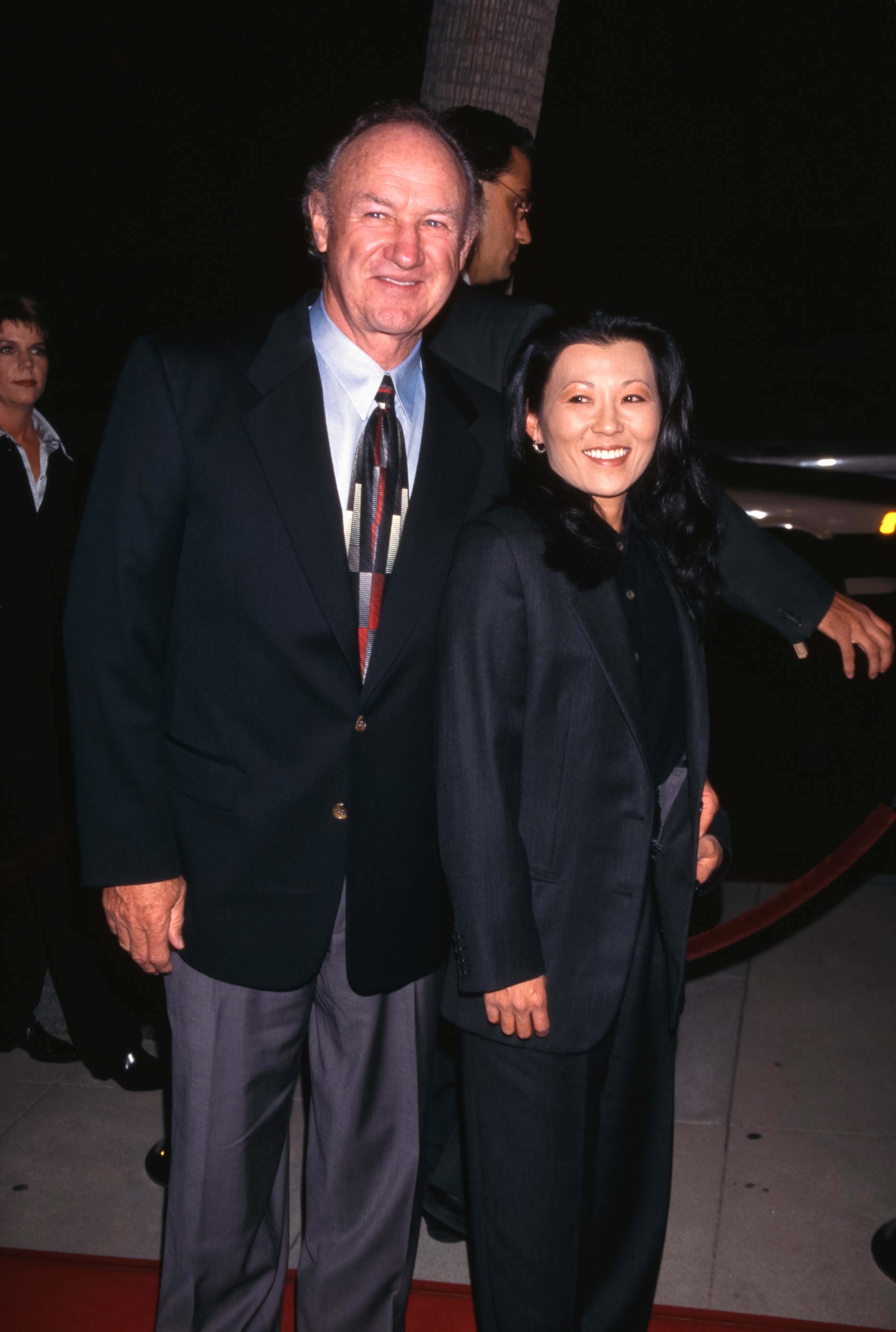 Gene Hackman in a black blazer and patterned tie, with Betsy Arakawa in a black outfit, at 