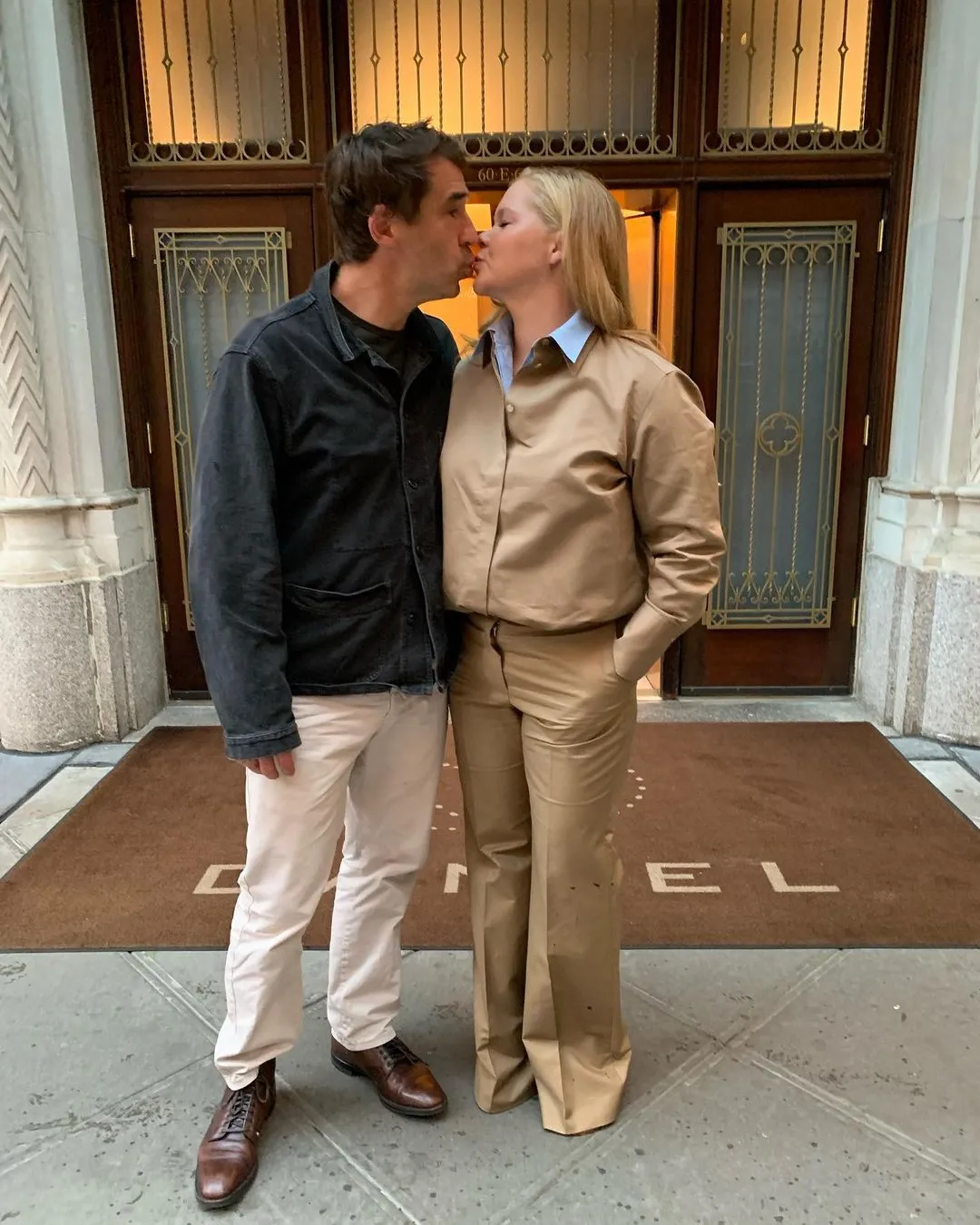 Amy Schumer and her husband Chris Fischer share a kiss outside a building.