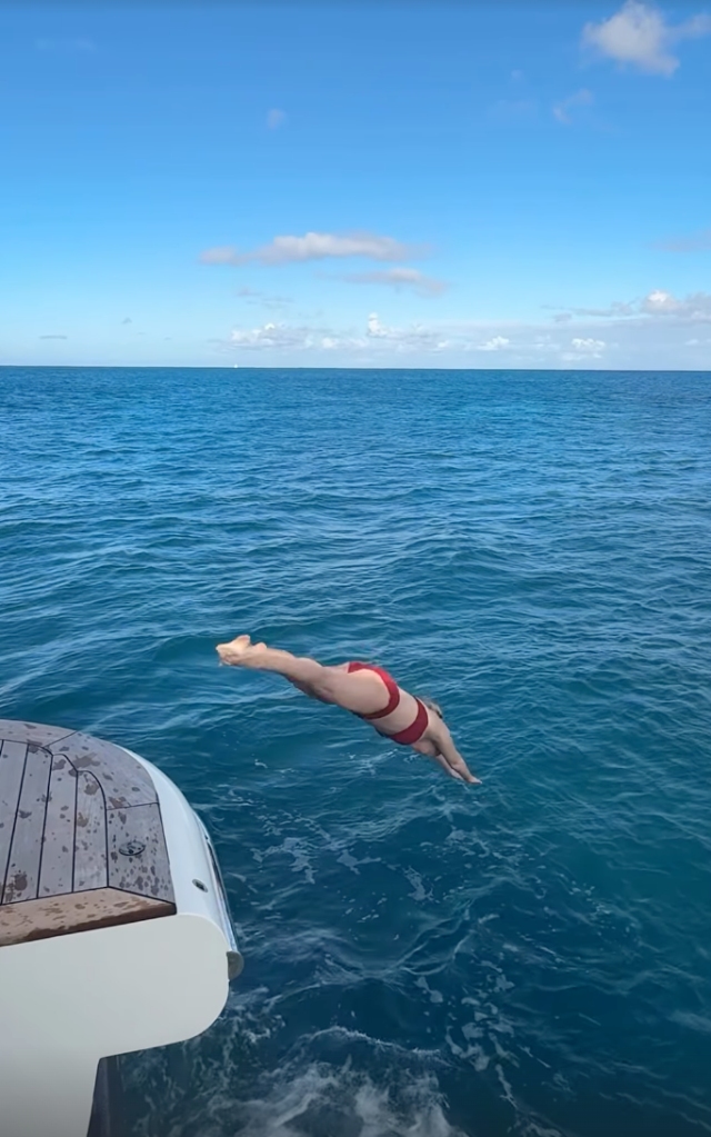 Amy Schumer in a red swimsuit diving off a boat into the blue ocean.