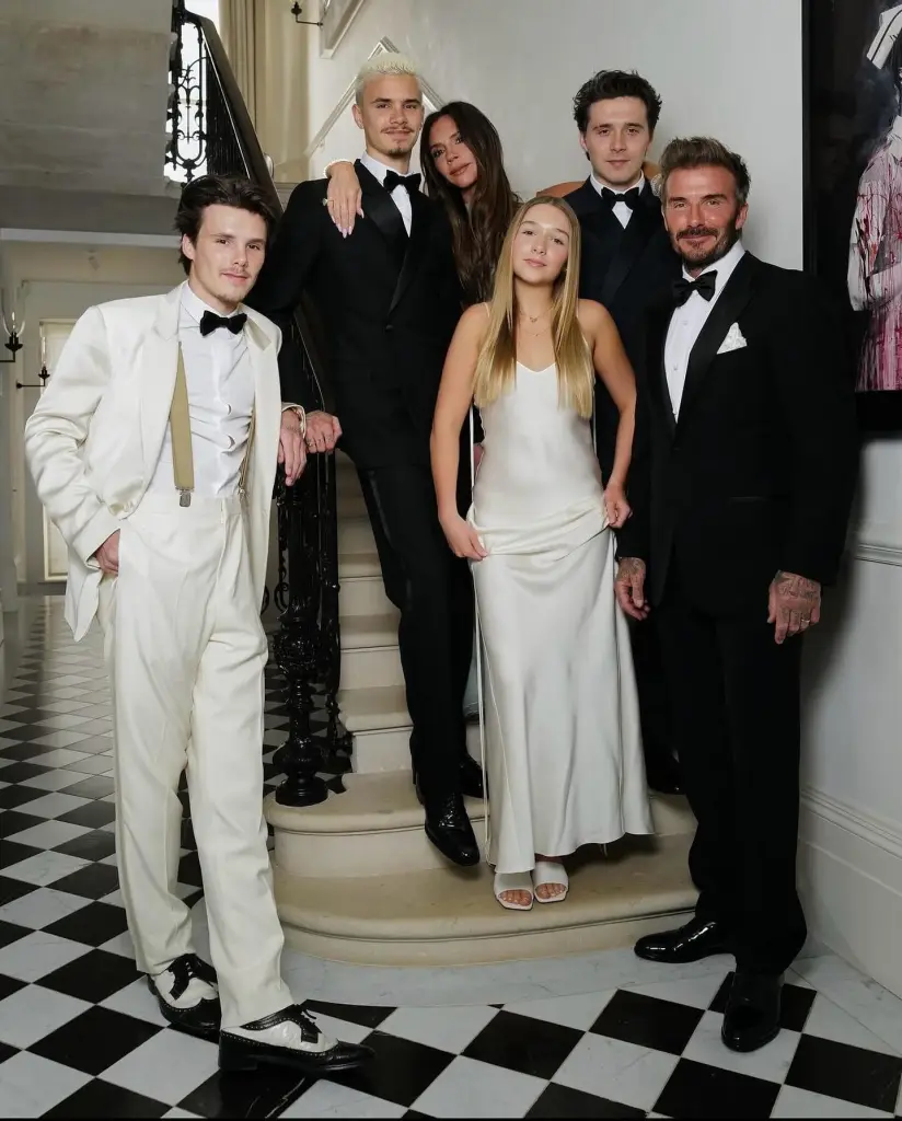 The Beckham family, including Victoria, David, Brooklyn, Romeo, Cruz, and Harper, dressed in formal wear on a staircase with a black and white checkered floor.