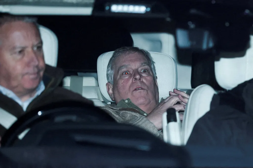 Andrew Mountbatten Windsor, also known as Prince Andrew, seated in the back of a vehicle with a second man driving.