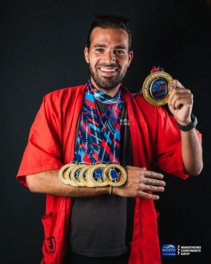 Anthony Simonetti holding medals for completing 7 marathons on 7 continents in 7 days.