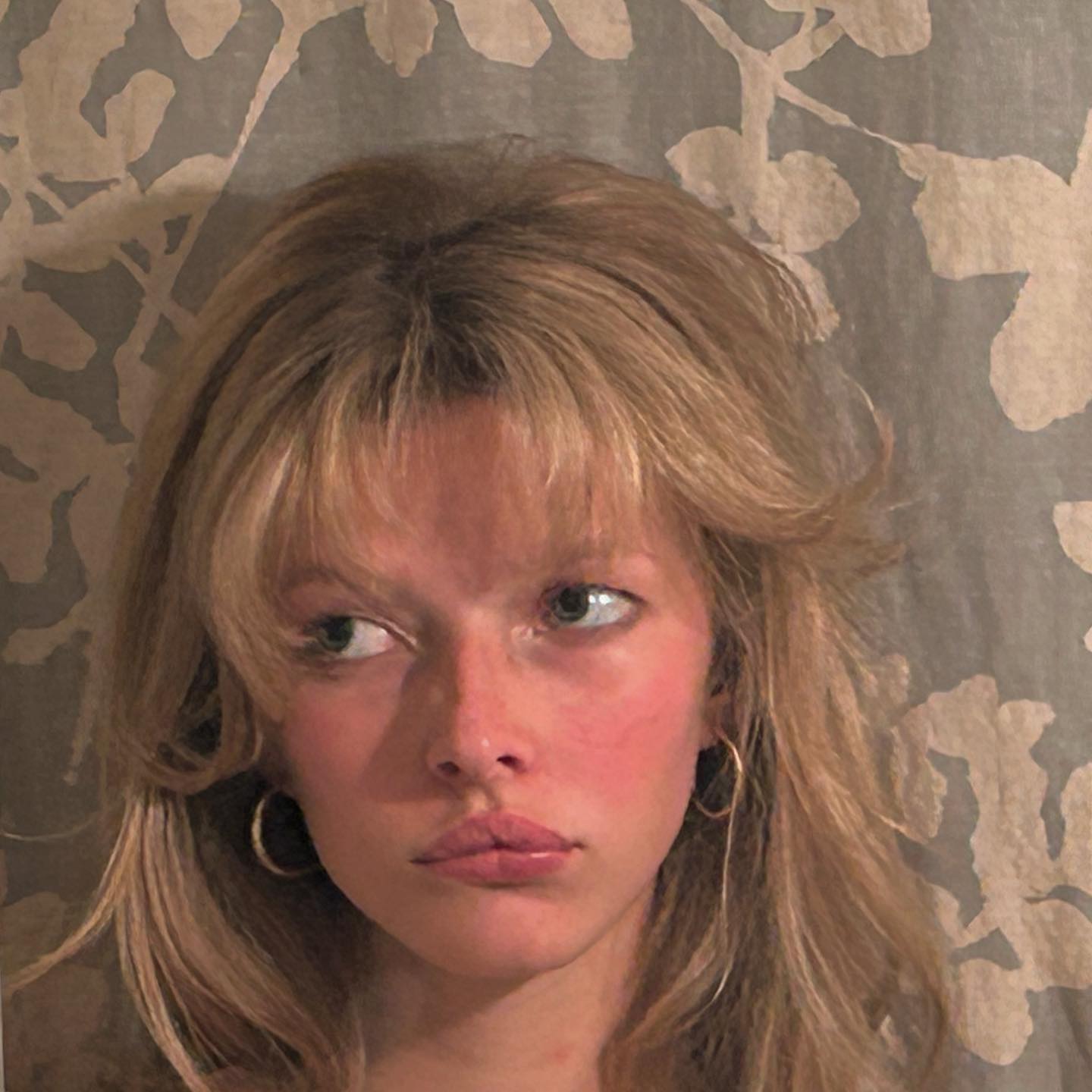 Apple Martin with blonde hair, golden hoop earrings, and flushed cheeks looking to the right.