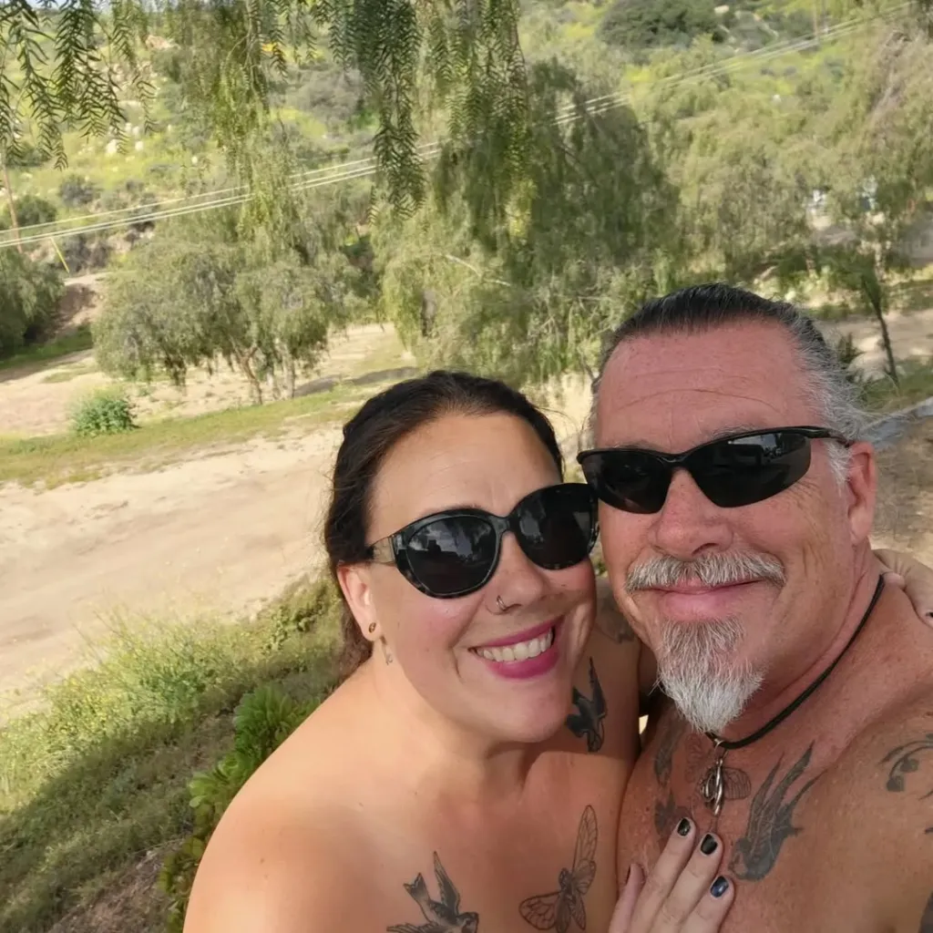 A couple in sunglasses smiles for a selfie at Olive Dell Ranch Nudist Resort.