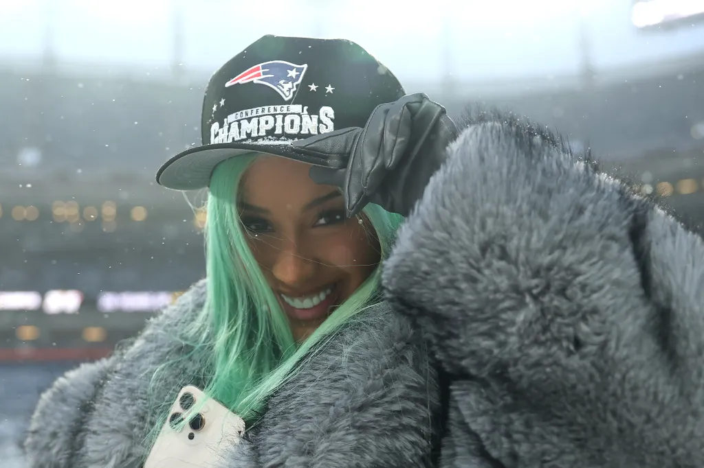 Cardi B smiles, wearing a Patriots 