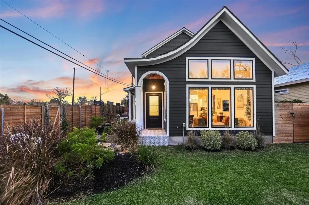 A dark-colored modern house with a front yard and a sunset sky.