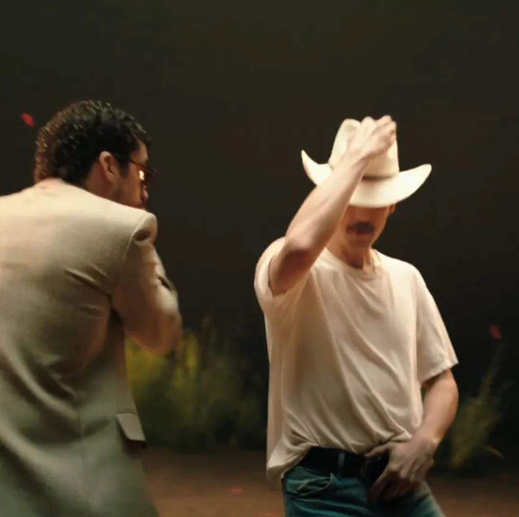 A person in a cowboy hat and white t-shirt dances with another person in a suit.