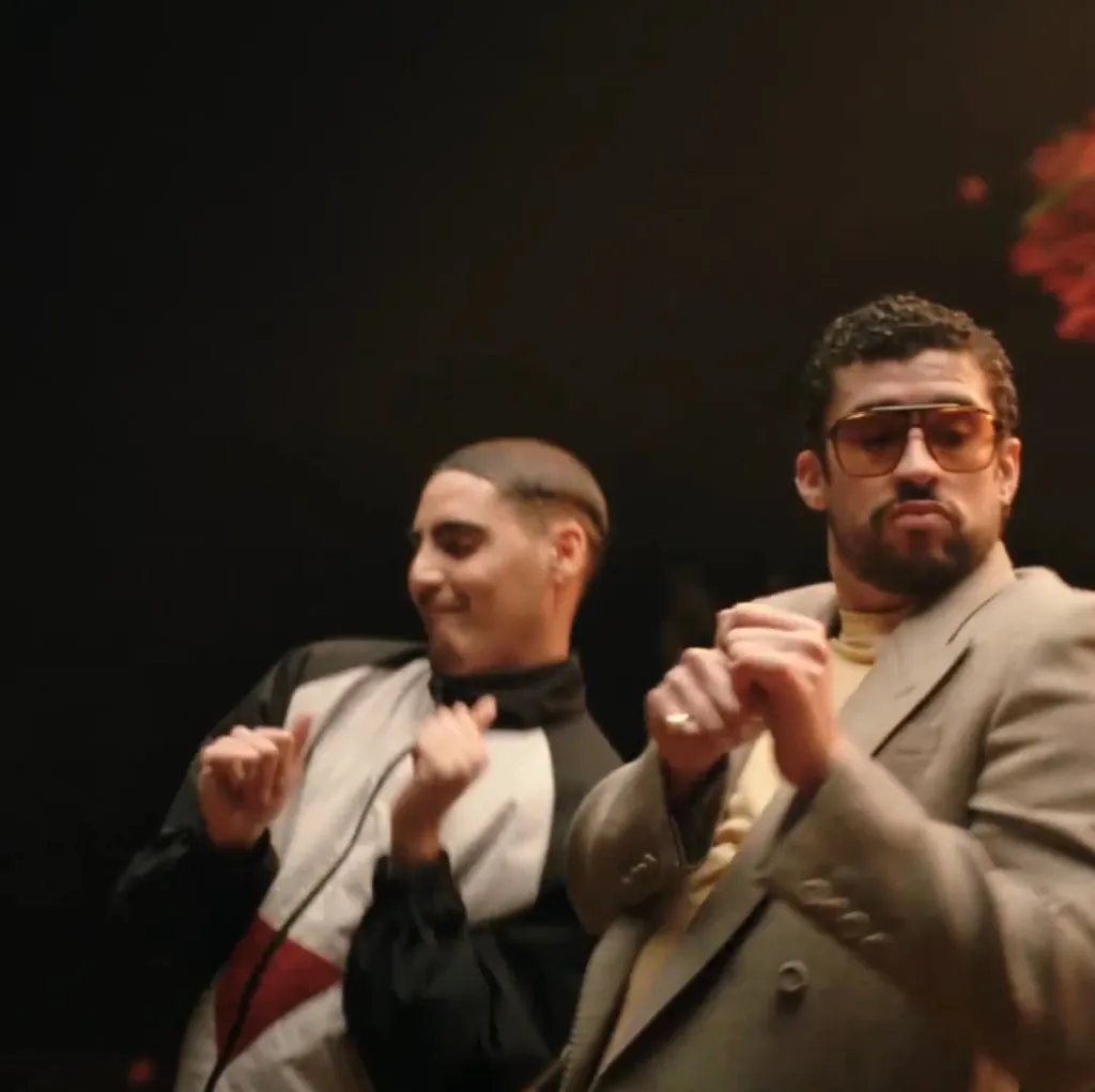 Bad Bunny dancing next to another person with their hands up in fists.
