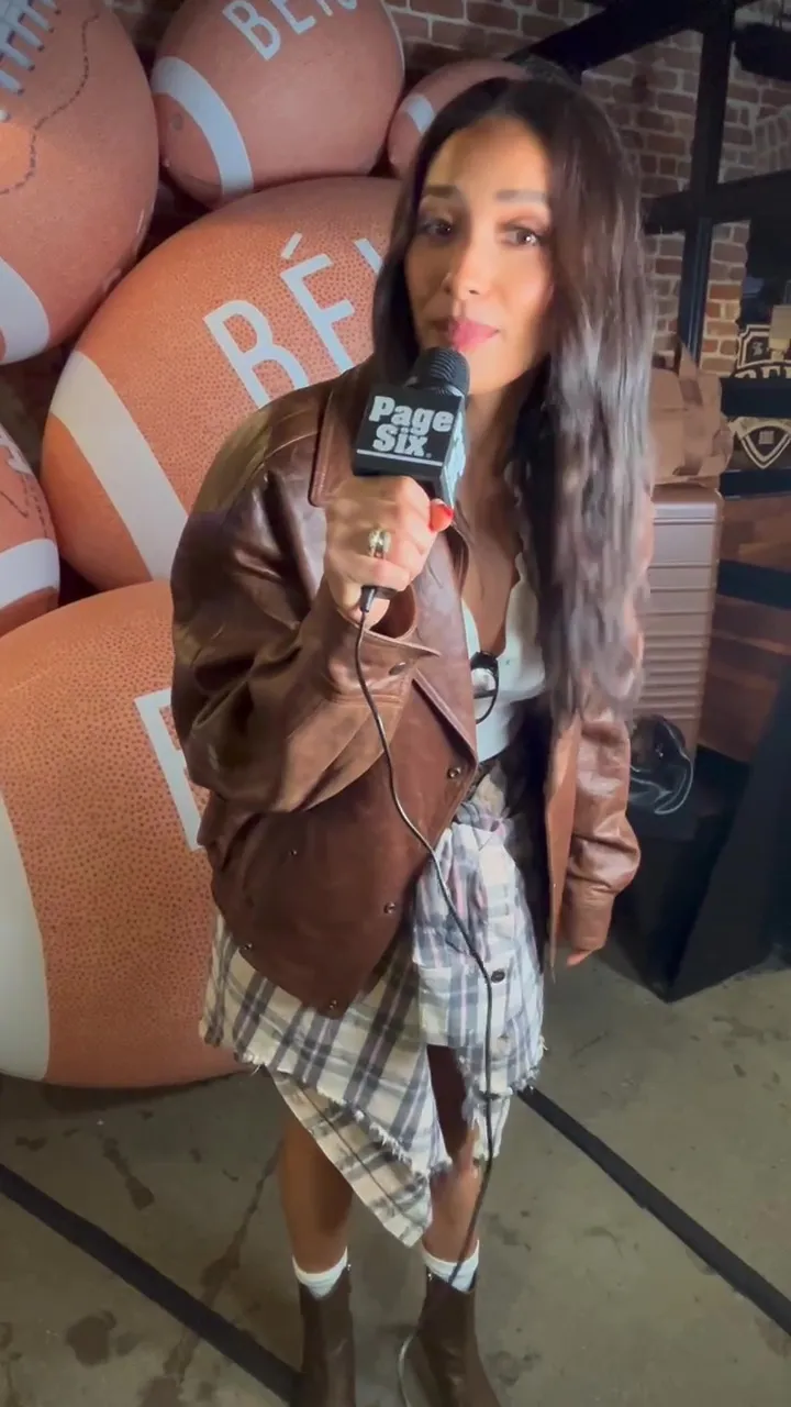 Shay Mitchell holds a Page Six microphone, standing in front of large football-shaped objects with 