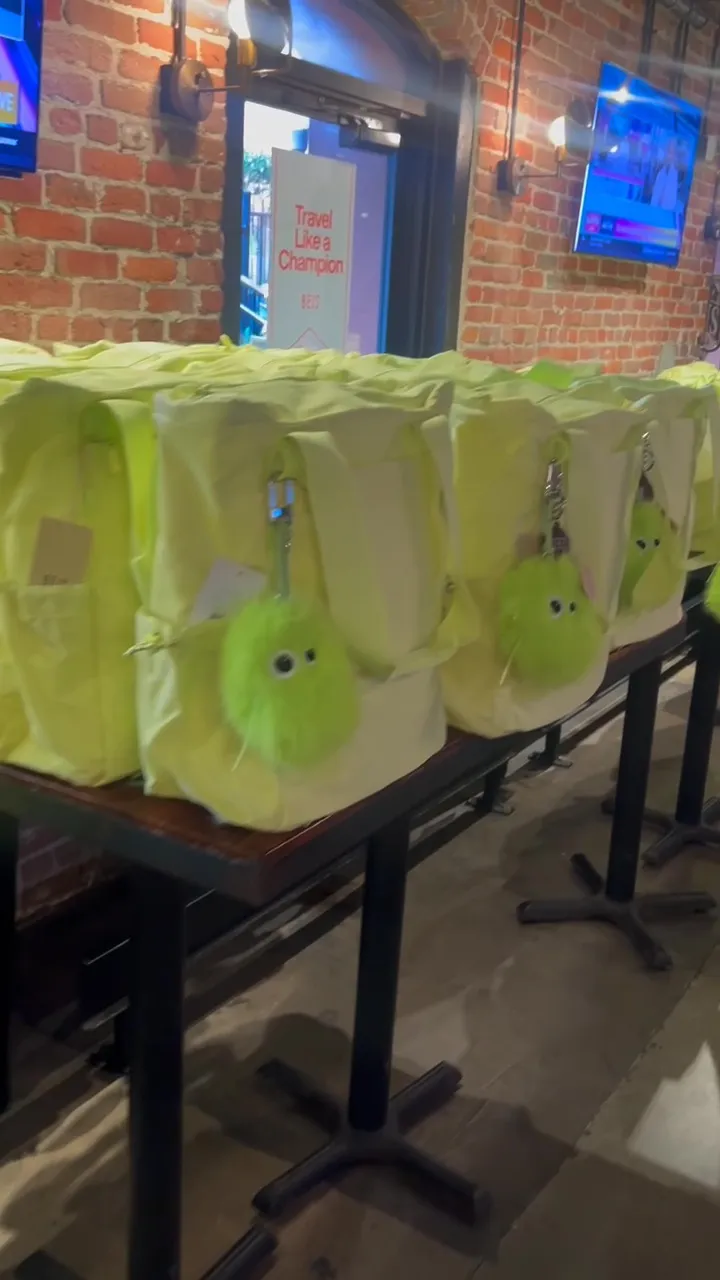 Lime green bags with furry keychains on tables in a brick-walled room.