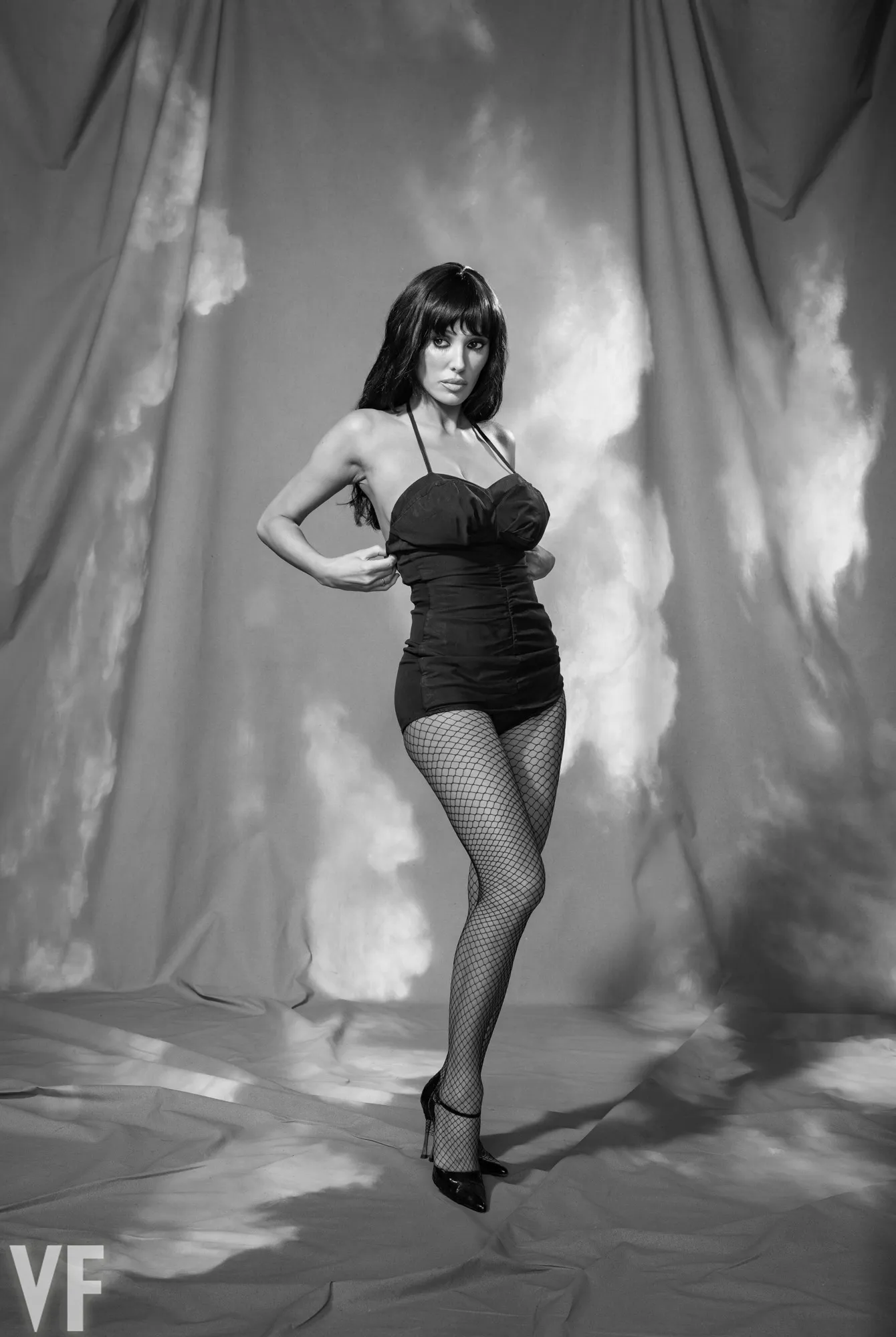 Bianca Censori in a black halter-neck swimsuit, fishnet stockings, and high heels.