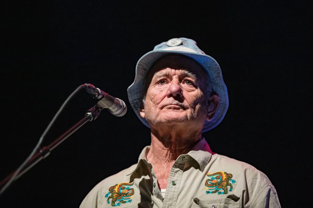 Bill Murray wearing a bucket hat and a shirt with a colorful embroidered lizard on stage.