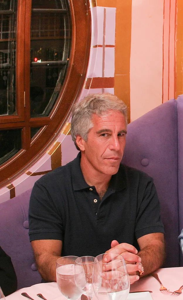 Jeffrey Epstein, a white man with graying hair, sits at a table in a dark polo shirt with his hands clasped.