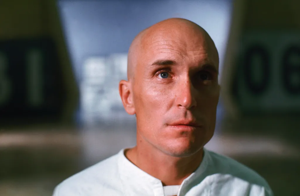Robert Duvall as THX 1138, bald, wearing a white uniform.