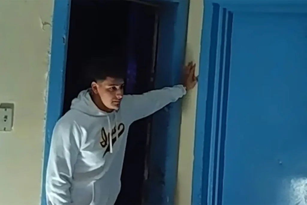 Bodycam footage of a young man in a white hoodie in a doorway.