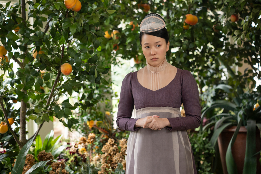 Yerin Ha as Sophie Baek from Bridgerton, looking concerned in a purple dress and small white hat.