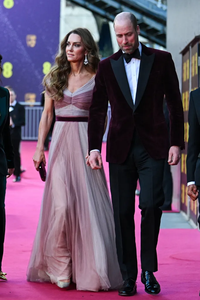 Catherine, Princess of Wales, in a pink gown, and Prince William, Prince of Wales, in a velvet suit, walk the pink carpet at the BAFTA Awards.