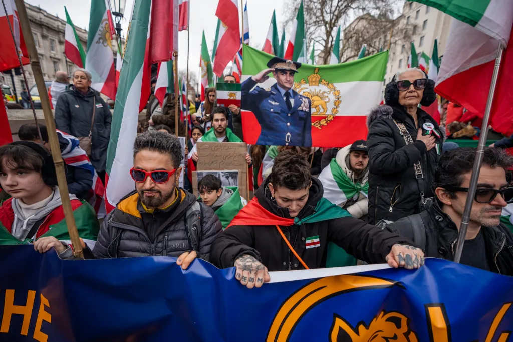 Protesters holding Iranian flags and a banner featuring a saluting military figure against an Iranian flag.