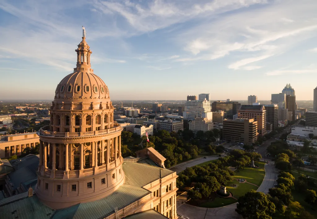 Aerial view of the Texas State Capitol Building in Austin, with the city skyline in the background under a blue sky.