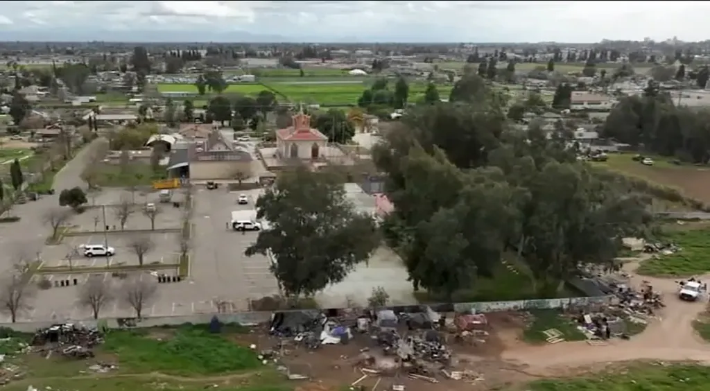 Aerial view of an urban landscape with a parking lot, buildings, trees, and an encampment.