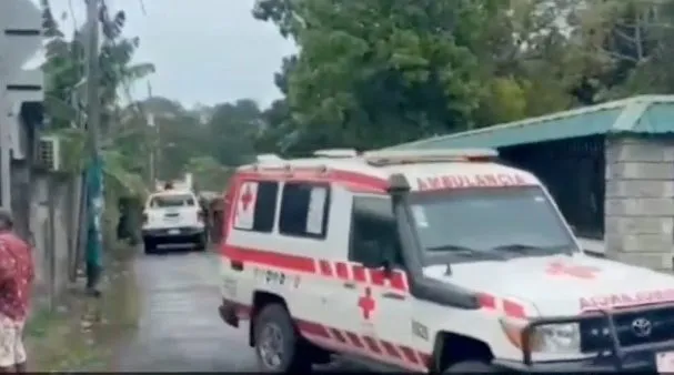 An ambulance is parked on a street where two men and a woman stand by a bicycle.