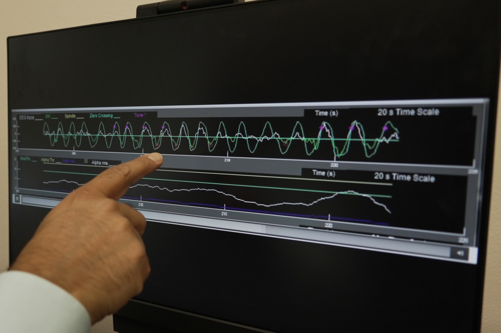 A hand points to a computer screen displaying an EEG trace and other brain wave frequencies.