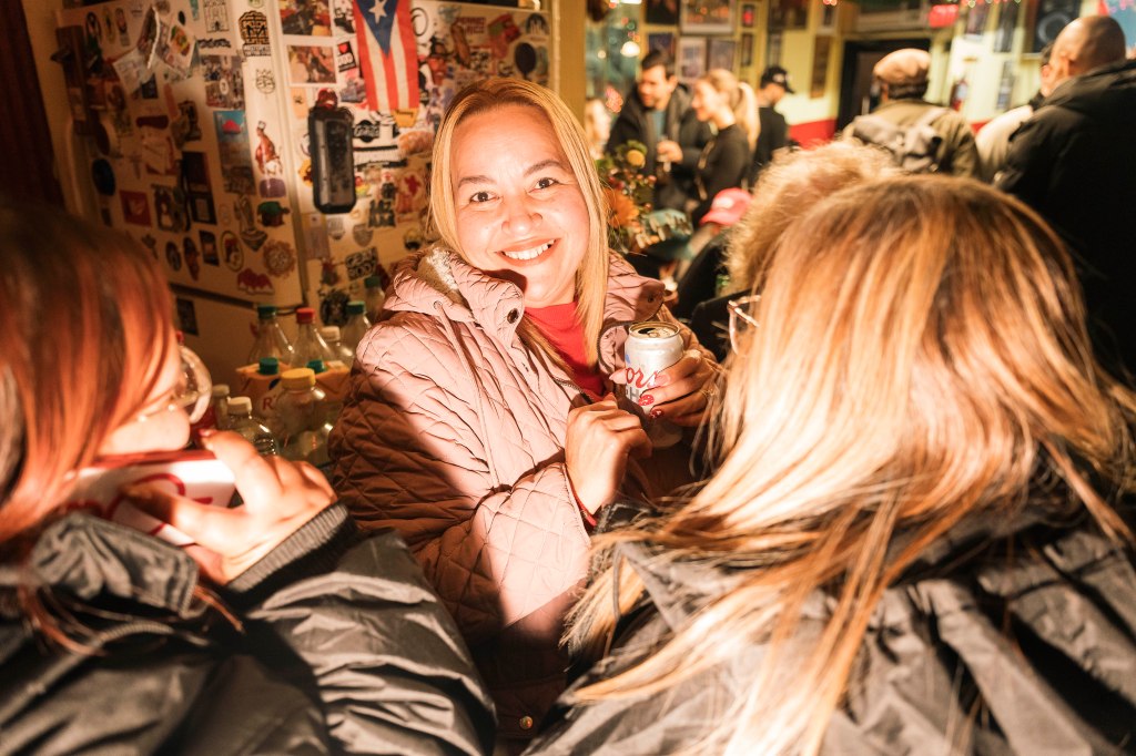 A smiling woman in a pink jacket holds a canned drink at the Caribbean Social Club.