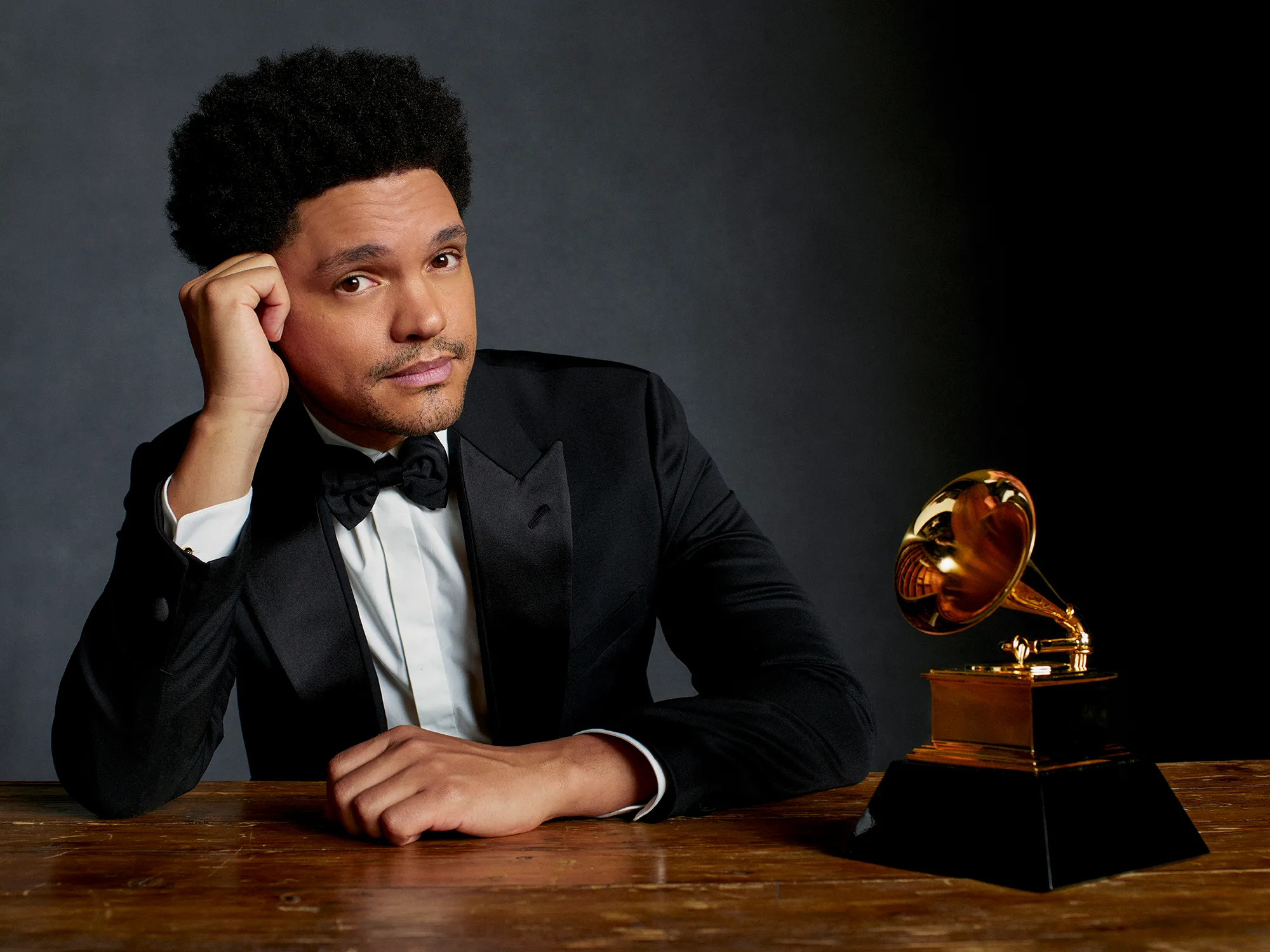 Trevor Noah in a poster for the Grammys with the gramophone next to him on a table