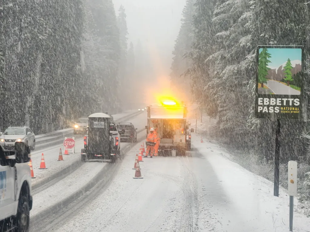 Snowfall on Ebbetts Pass with orange cones, vehicles, and workers.