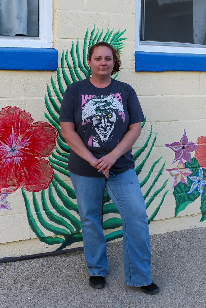 Chevy, 36, stands in front of a mural with painted flowers and palm fronds.