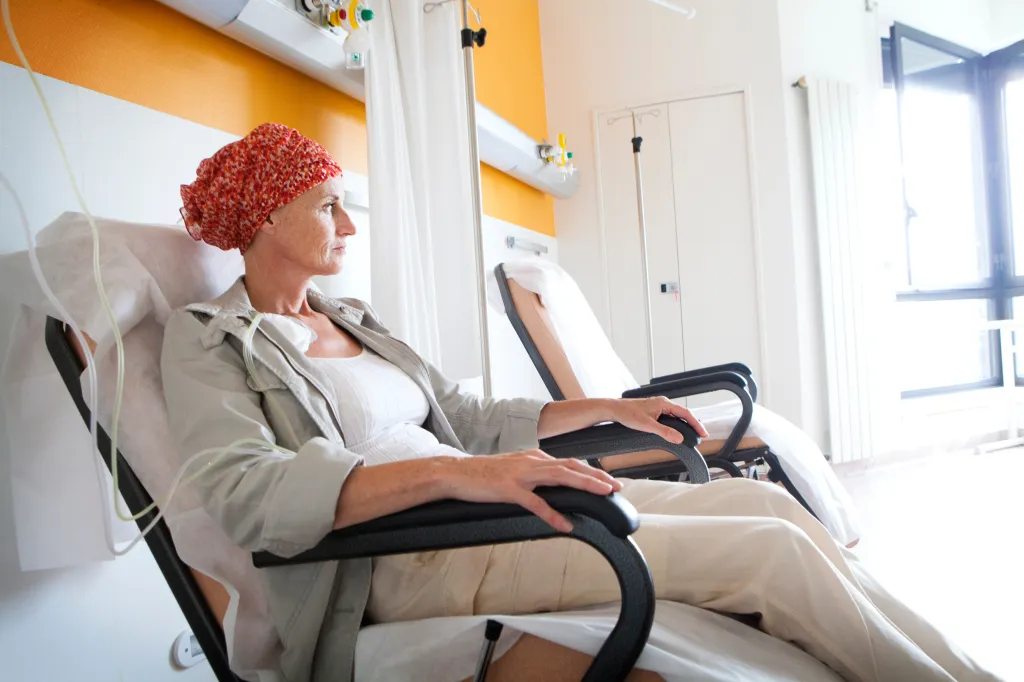 A woman wearing a red headscarf sits in a chair receiving ambulatory chemotherapy.