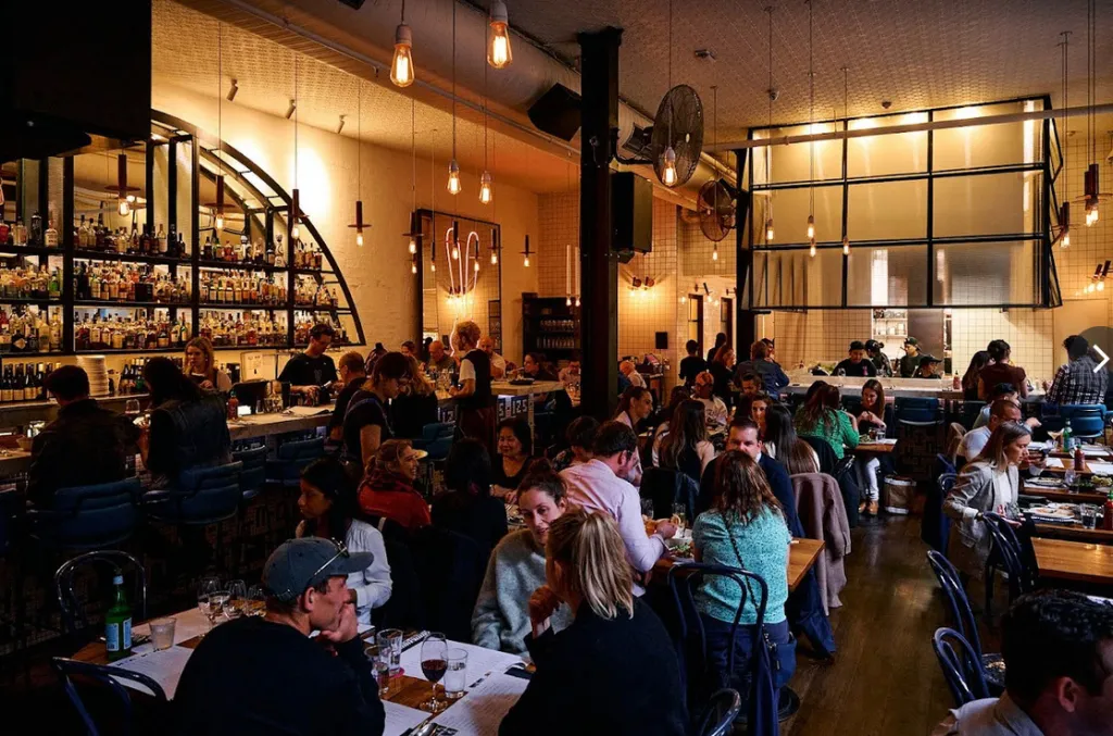 A busy diner with a full bar on the left, and many people seated at tables and the bar.