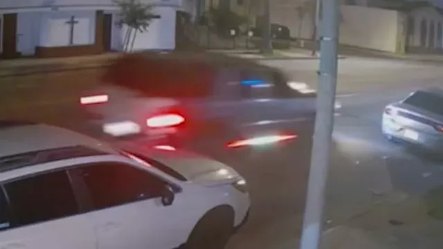 A blurry image of a dark car with its brake lights illuminated, driving past a white car at night.