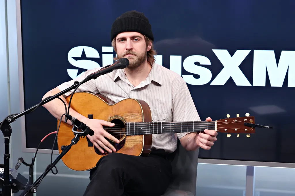 Christian Lee Hutson playing an acoustic guitar and singing into a microphone at SiriusXM Studios.