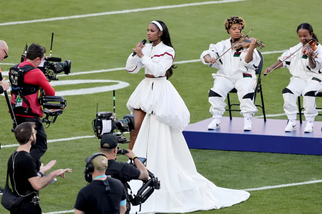 Coco Jones performing during the Super Bowl LX, with two violinists and cameramen in the background.