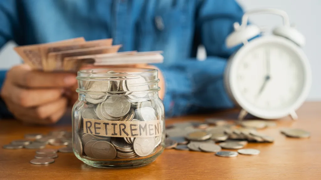 A person putting money into a glass jar labeled 